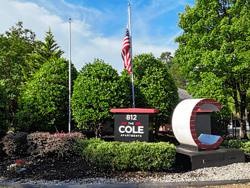 A sign for Cole Apartments is in front of a green hedge and a flag pole.