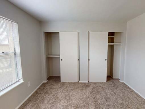 A room with white walls and carpeted floor with three white doors.