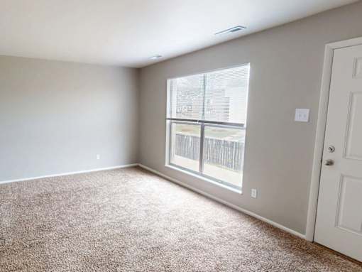 A room with a carpeted floor and a window with blinds.