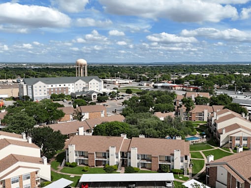A large white building with a tower is surrounded by smaller buildings and trees.