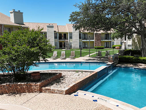 A pool surrounded by a brick wall and a tree.