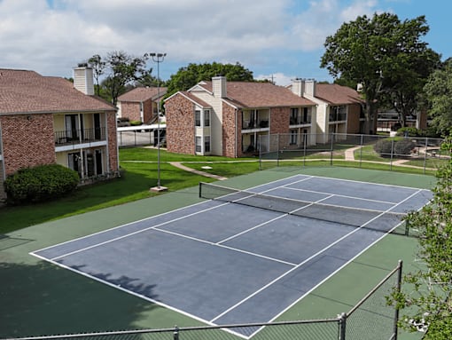 A tennis court is surrounded by a fence and a grassy area.