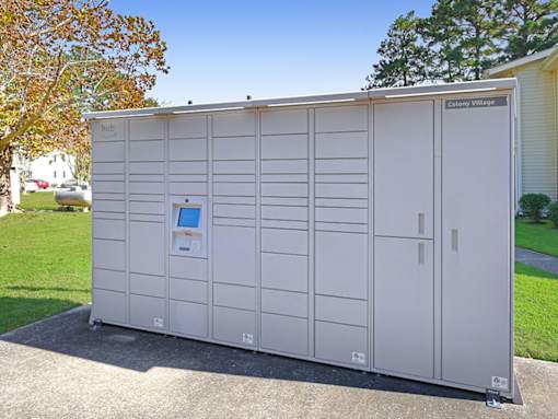 A portable toilet is parked on a concrete slab outside a Colony Village building.