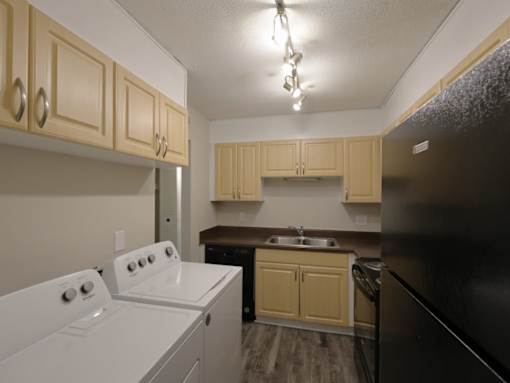 In-home washer and dryer in kitchen area with oven and a black refrigerator.