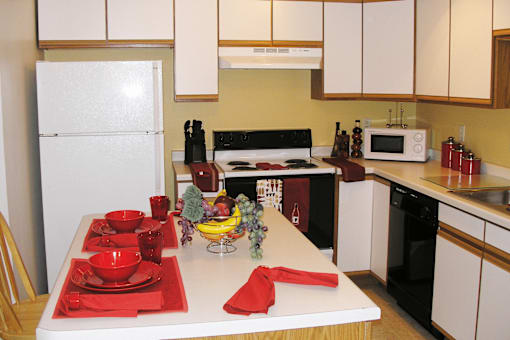 A kitchen with a white fridge, a white table with red napkin and red bowls.