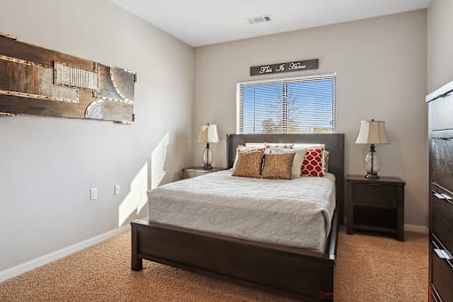 A bedroom with a bed, two lamps, and a painting on the wall.