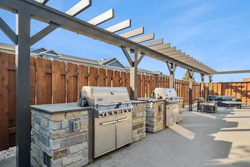 A row of outdoor kitchen appliances are lined up under a pergola.