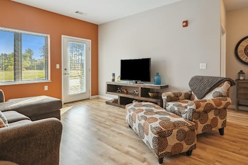 A living room with a grey sofa, a brown armchair, and a patterned ottoman.