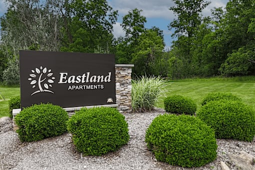 A sign for Eastland Apartments is surrounded by green bushes.