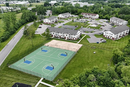 A basketball court is surrounded by a fence and is located in a grassy area.