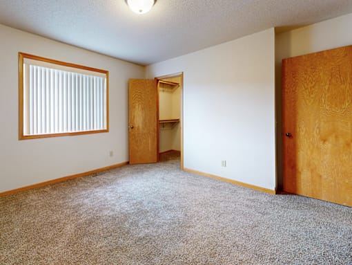 A room with a carpeted floor, a window with blinds, and a wooden door.