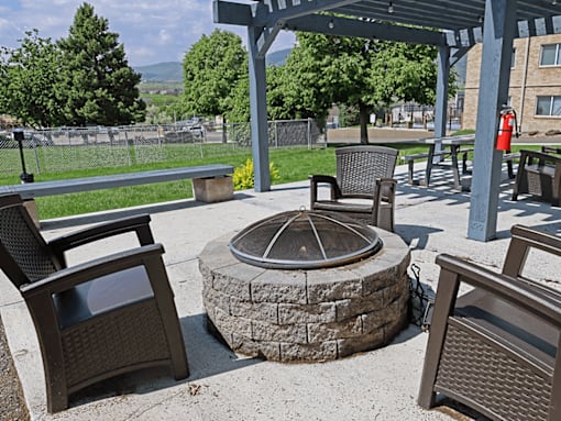 A patio with a fire pit and chairs.