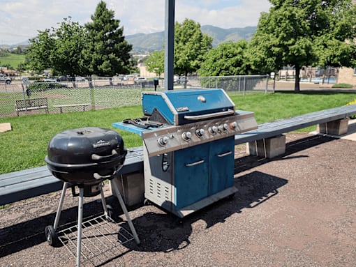 A blue grill is on a picnic table outside.