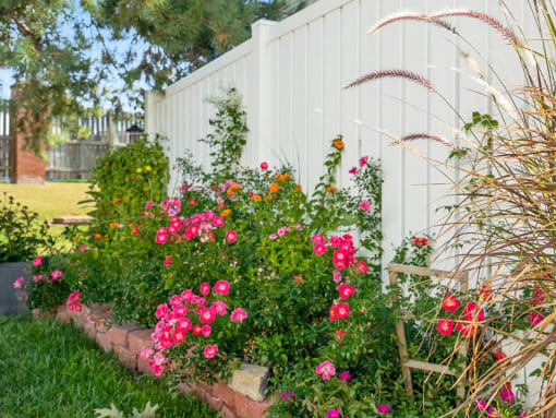 a flower garden in front of a white fence