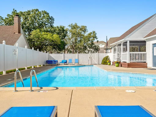 a swimming pool in front of a house with a white fence