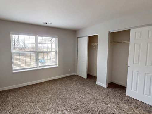 A room with a carpeted floor, two white doors, and a window with blinds.