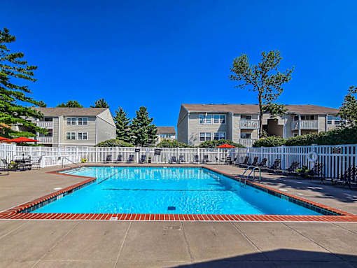 A swimming pool surrounded by a white fence and apartment buildings.
