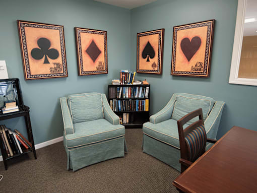 A room with two chairs and three framed pictures of playing cards on the wall.