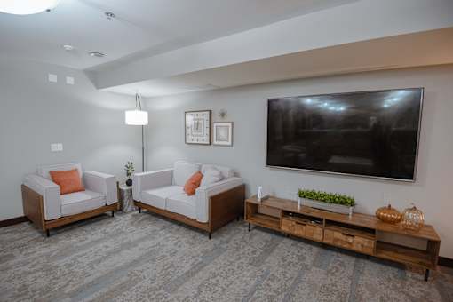 A living room with a grey carpet and a television on the wall.