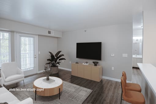 A living room with a white chair, a brown chair, a white sofa, a wooden coffee table, a flat screen TV, and a plant.