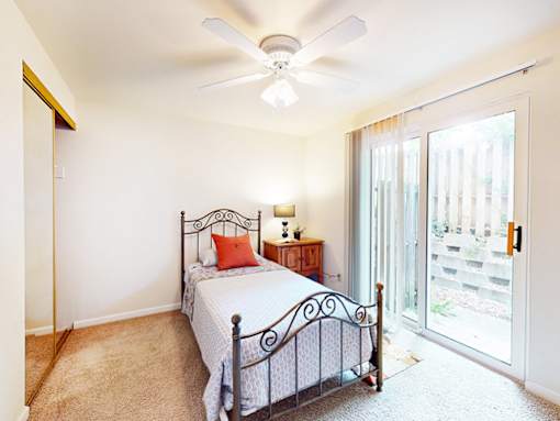 A bedroom with a bed, a ceiling fan, and a sliding glass door.