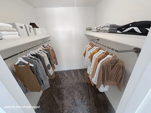 A white closet with clothes hanging on hangers.