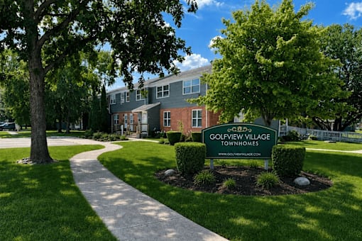 A sign for Golfview Village Townhomes is in the foreground of a well kept lawn.