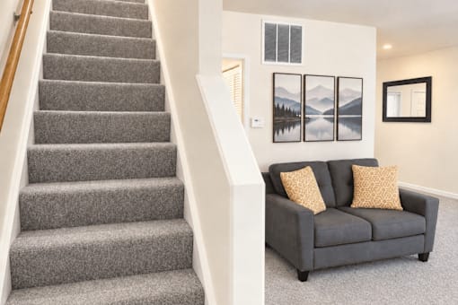 A grey couch with two pillows sits in front of a wall with three pictures hanging on it.