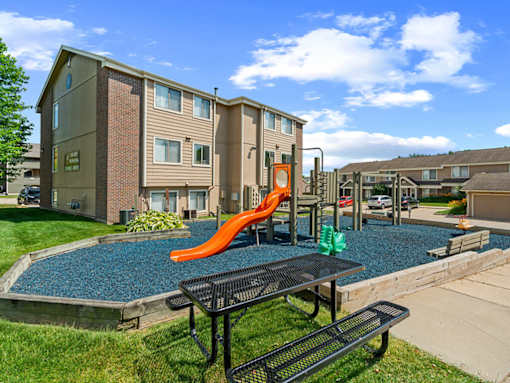 A playground area with a slide and picnic table in front of apartment buildings.