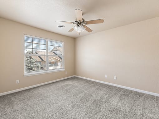 A room with a ceiling fan and a window showing a view of a house.