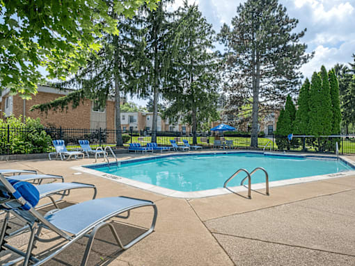A pool surrounded by trees and chairs.