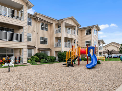 A playground with a blue slide and yellow climbing frame in front of apartment buildings.