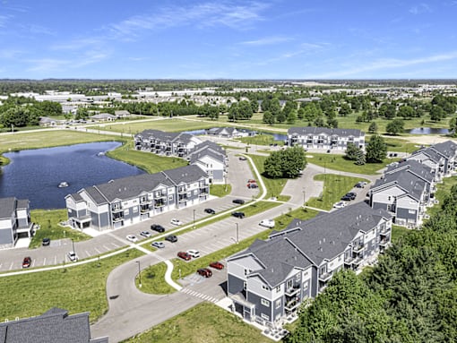 A bird's eye view of a residential area with houses, cars, and a lake.