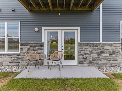 Two chairs are placed on a concrete slab outside a house.