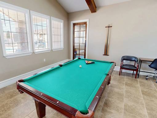 A pool table in a room with a chair and a window.