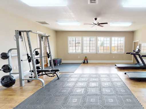 A spacious home gym with a weight bench, treadmill, and a ceiling fan.