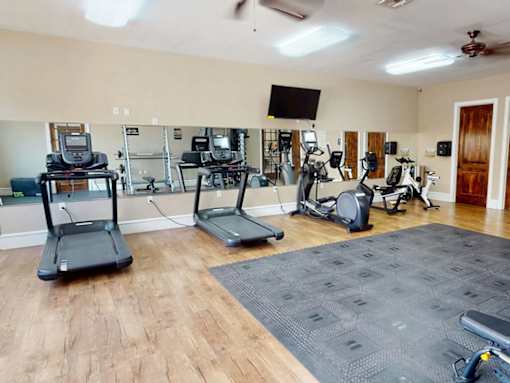 A gym with treadmills, elliptical machines, and a television.