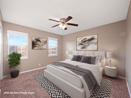 A bedroom with a large bed, a ceiling fan, and a potted plant.