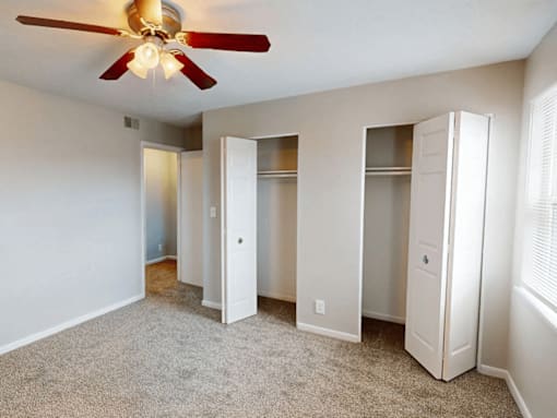 A room with a ceiling fan and three closets.