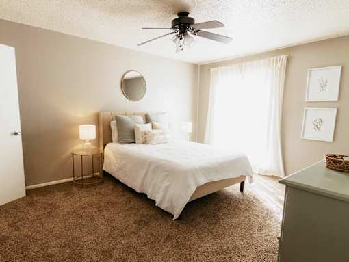 A bedroom with a bed, a ceiling fan, and a carpeted floor.