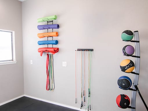 A wall of exercise equipment including a rowing machine, a wall mounted pull up bar, and a row of resistance bands.