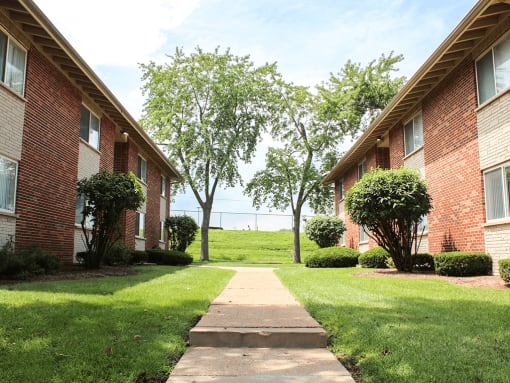 a walkway between two apartment buildings with grass and trees