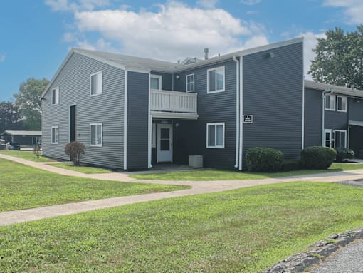 A grey two story apartment building with a balcony on the second floor.