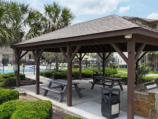 A pavilion with picnic tables and a fire pit is surrounded by greenery.