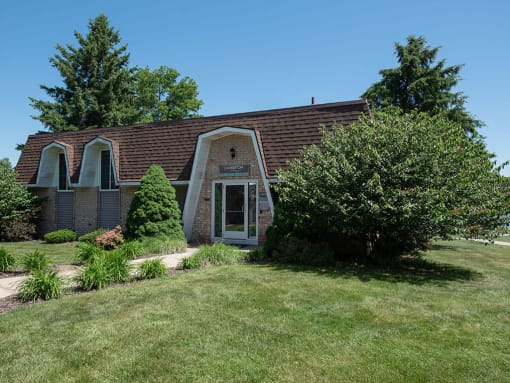 brick leasing office with a grassy yard and a tree