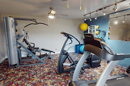 A gym with a variety of equipment including a leg press machine, a rowing machine, and a stationary bike.