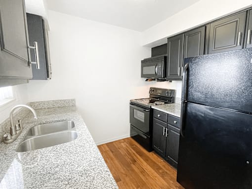 A kitchen with a black refrigerator, sink, and cabinets.