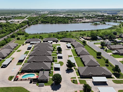 A bird's eye view of a residential area with houses, a swimming pool, and a river in the background.
