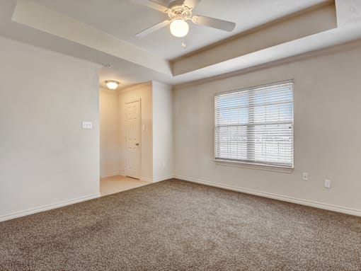 A room with a carpeted floor, a ceiling fan, and a window with blinds.