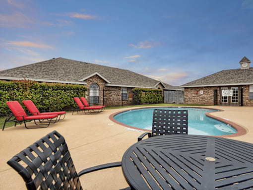 A black table and chairs are in the foreground of a backyard with a pool and a house in the background.
